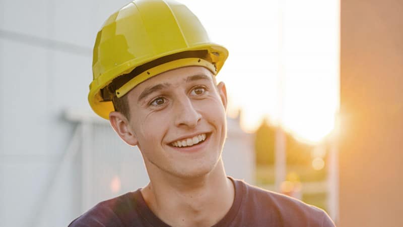 Lehre bei HABAU: Lehrling beim Verputz Junger Mann mit Bauhelm beim Verputz auf der Baustelle