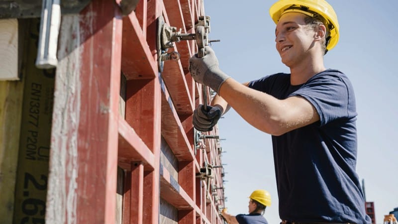 Junger Mann mit Bauhelm bei der Betonbau-Arbeit